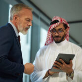 Medium shot of two Middle Eastern and Caucasian managers checking information in Internet on digital tablet