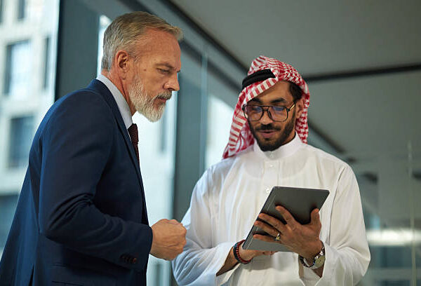 Medium shot of two Middle Eastern and Caucasian managers checking information in Internet on digital tablet