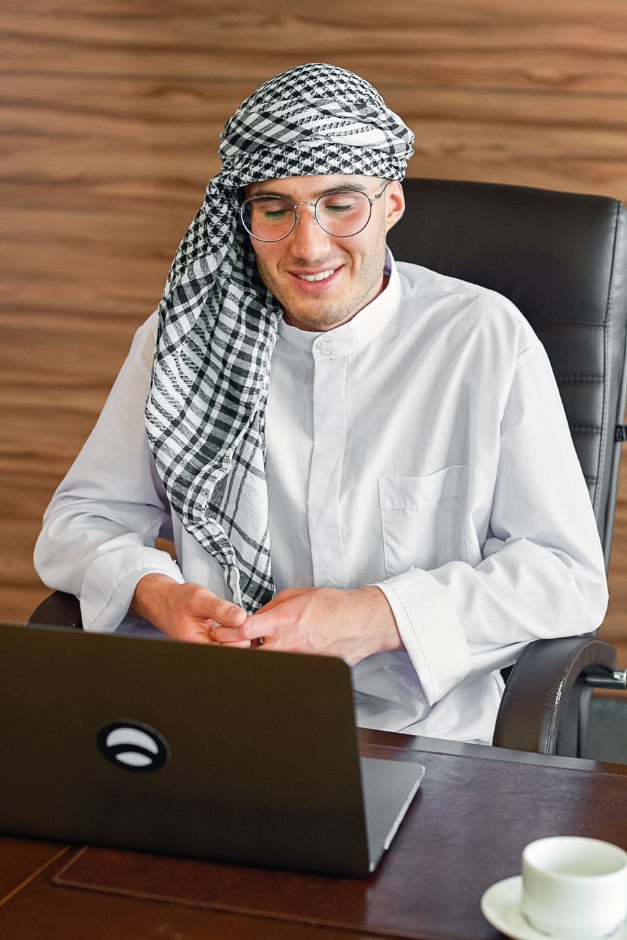 Emirati business owner smiling while working on a laptop